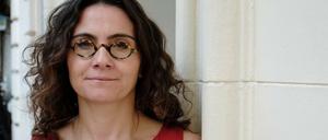 Eine Frau in einem roten Kleid steht lächelnd an eine Hauswand gelehnt.