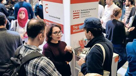 Bei einer Messe stehen junge Männer an einem Messestand und sprechen mit einer Frau.