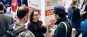 Bei einer Messe stehen junge Männer an einem Messestand und sprechen mit einer Frau.