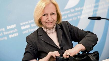 Eine Frau lächelt in die Kamera und hantiert mit ihrer Handtasche.