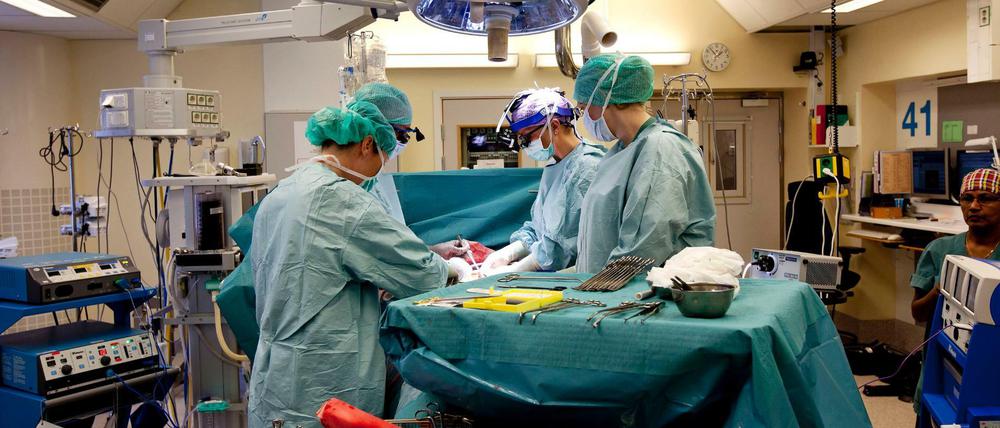 Männer in blau-grünen Kitteln stehen an einem Operationstisch.