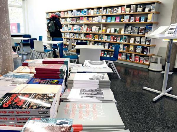 Zu sehen ist ein Büchertisch, im Hintergrund ein langes Regal, vor dem eine Besucherin steht.