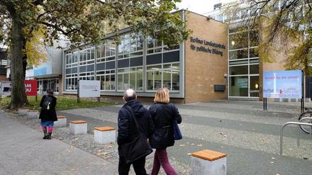 Passanten gehen an einem Gebäude vorbei und blicken in Richtung eines Plakats mit der Frage "Kennst du die schon?".