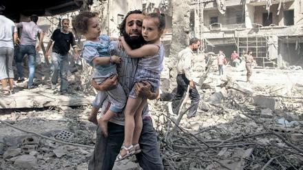 Ein Syrer trägt seine beiden Töchter durch die Ruinen von Aleppo. 