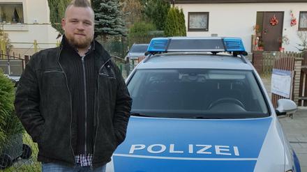 Maximilian Kraft von der Firma Blue and White posiert vor einer Streifenwagen-Attrappe. 