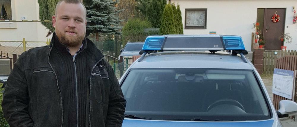 Maximilian Kraft von der Firma Blue and White posiert vor einer Streifenwagen-Attrappe. 