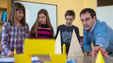 Drei Kinder und eine Lehrkraft arbeiten mit geometrischen Figuren.