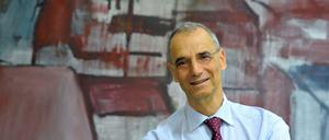 Ein Mann steht lächelnd vor einem Gemälde, das eine Stadtlandschaft zeigt.