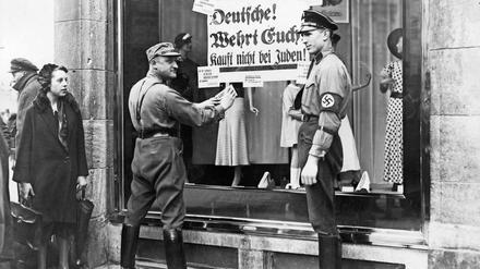 Am Anfang stand die Ausgrenzung: Ein SA- und SS-Mann bekleben 1933 in Berlin das Schaufenster eines Textilgeschäftes mit Boykott-Plakaten.