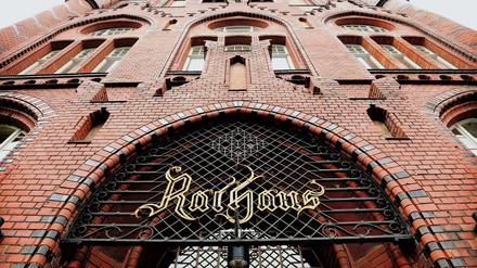 Portal und rote Backsteinfassade des Rathauses Lichtenberg mit historischem "Rathaus"-Schild am Gitter.