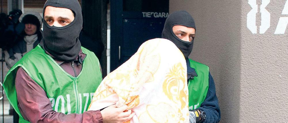 Polizisten führen bei einer Razzia gegen Islamisten am 04.02.2016 in Berlin einen mit einem Tuch verdeckten Verdächtigen ab.