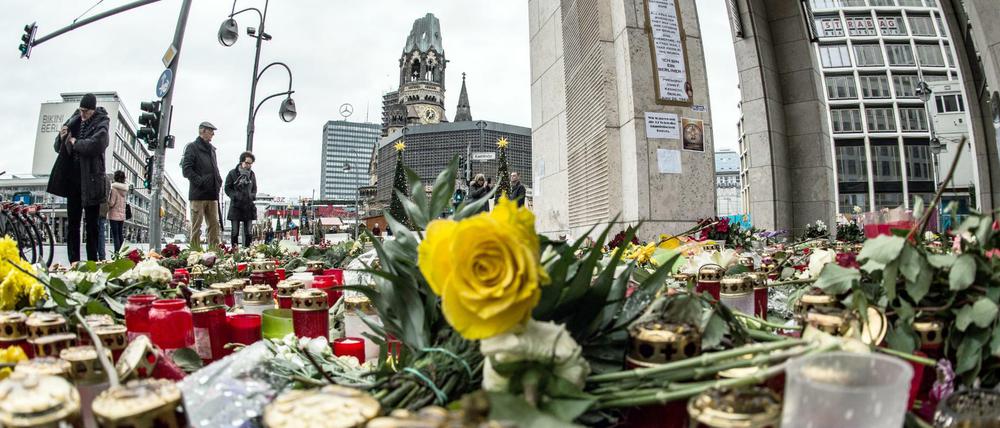 Passanten stehen am 26.12.2016 in Berlin vor einem Blumen- und Kerzenmeer am Breitscheidplatz, dem Ort des Anschlags.