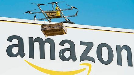 Eine Drohne mit einem Amazon-Paket schwebt vor dem Amazon Logistikzentrum Leipzig.