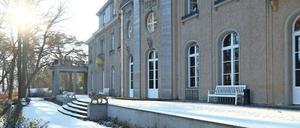 Die Fassade einer Villa im Gegenlicht fotografiert, davor schneebedeckte Gartenanlagen.