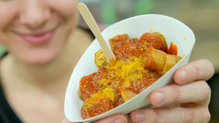 Junge Frau hält Schälchen mit veganer Currywurst in die Kamera.