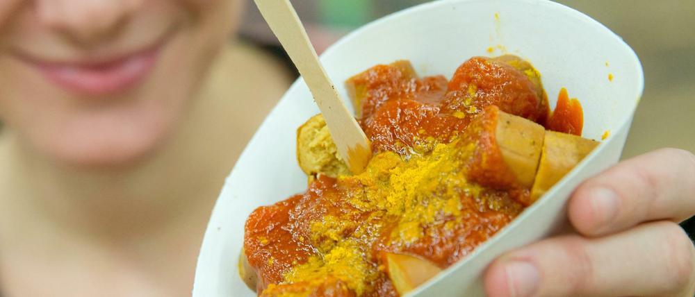 Junge Frau hält Schälchen mit veganer Currywurst in die Kamera.