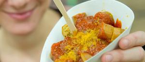 Junge Frau hält Schälchen mit veganer Currywurst in die Kamera.