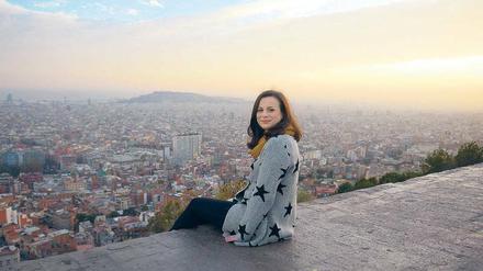Eine junge Frau sitzt auf einer Terrasse mit Blick auf eine große Stadt.