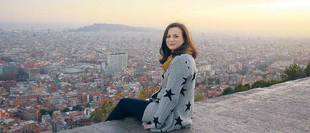 Eine junge Frau sitzt auf einer Terrasse mit Blick auf eine große Stadt.