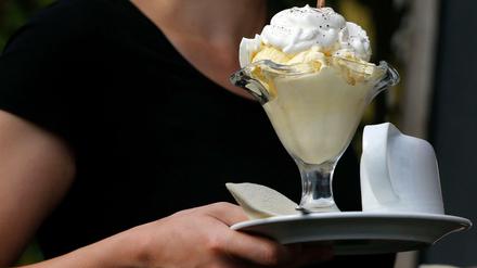 Eine Servicekraft serviert in einer Gaststätte einen Eisbecher.