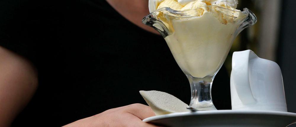 Eine Servicekraft serviert in einer Gaststätte einen Eisbecher.