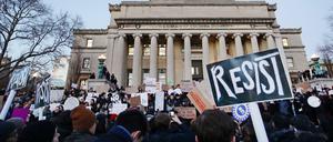 Vor einem historischen Universitätsgebäude stehen junge Menschen, die Plakate mit Aufschriften wie "Resist" hochhalten.