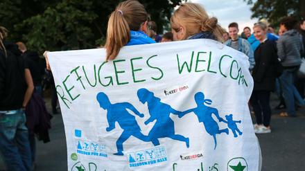 Zwei junge Frauen sind in ein Banner mit der Aufschrift Refugees welcome gehüllt.