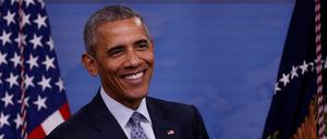 Ex-US-Präsident Barack Obama steht lächelnd vor einer amerikanischen Flagge.