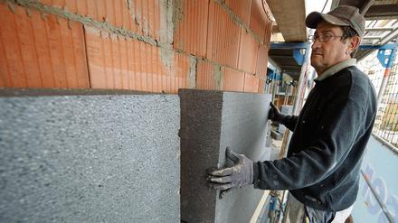 Dämmen für den Klimaschutz: Ein Handwerker montiert eine Styroporplatte zur Wärmedämmung an die Fassade eines Mehrfamilienhauses in Straubing (Niederbayern). 