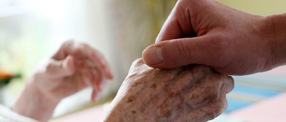 Ein Pfleger hält in einem Alten-und Pflegeheim die Hand einer Bewohnerin.