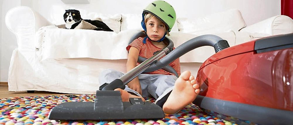 Ein Junge mit einem Fahrradhelm auf dem Kopf sitzt in schlaffer Haltung vor einem Staubsauger auf dem Boden.