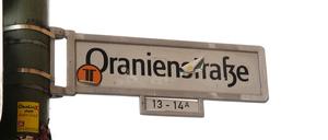 Ein Straßenschild der Oranienstraße. Radfahrer sind gefährdet, Busse fahren langsam und Fußgänger kommen nicht rüber.