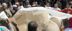 Männer und Frauen bedecken eine monumentale Statue mit Stoffbahnen.