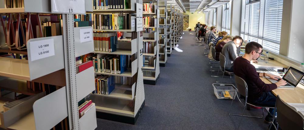 Studierende und wissenschaftliche Mitarbeiter sitzen in einer Bibliothek an ihren Laptops.