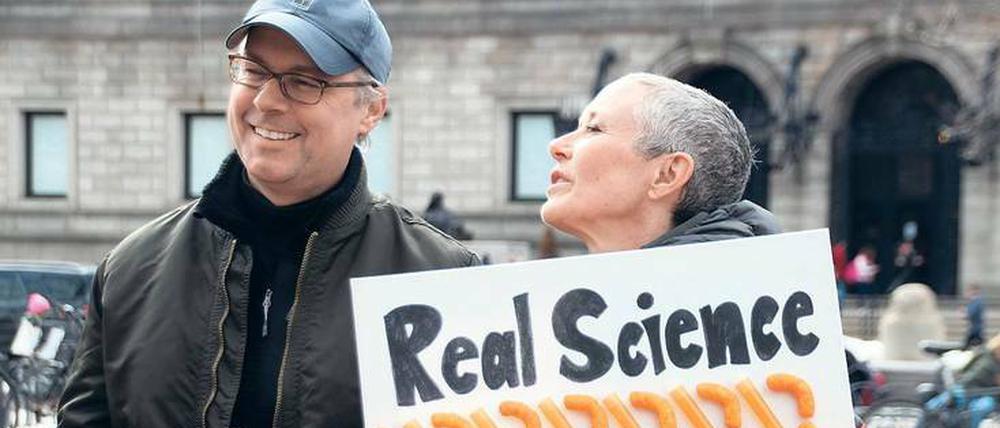 Eine Frau steht auf der Straße mit einem Schild auf der Hand, darauf steht: Real Science, Fake President.