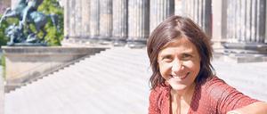 Eine Frau sitzt vor einem Museumsbau in der Sonne und lächelt.