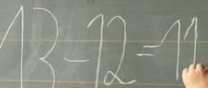 Ein Junge schreibt eine einfache Gleichung an die Tafel.