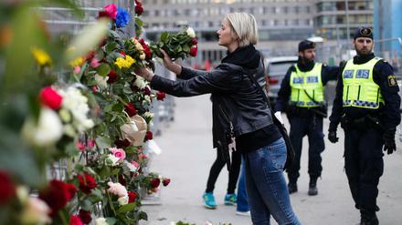Eine Frau steckt am Ort des Anschlags Blumen in einen Zaun. 