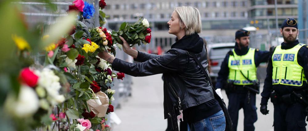 Eine Frau steckt am Ort des Anschlags Blumen in einen Zaun.