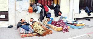 Junge Männer campieren auf dem Fußweg vor einem Gebäude auf Matratzen.