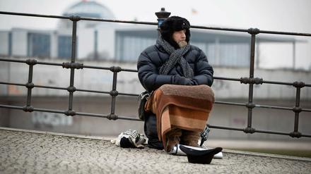 Udo, ein Obdachloser, sitzt im Winter in Berlin an der Spree im Regierungsviertel und bittet um Unterstützung.