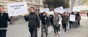 Studierende tragen Plakate und Grableuchten über einen Uni-Campus.