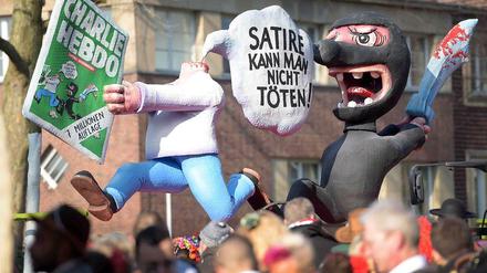 "Satire kann man nicht töten", steht in einer Sprechblase. Zu sehen sind eine Figur ohne Kopf, welche eine Ausgabe des Satiremagazins "Charlie Hebdo" in den Händen hält, und ein schwarz gekleideter "Terrorist" mit Schwert.