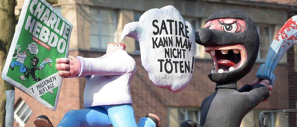 "Satire kann man nicht töten", steht in einer Sprechblase. Zu sehen sind eine Figur ohne Kopf, welche eine Ausgabe des Satiremagazins "Charlie Hebdo" in den Händen hält, und ein schwarz gekleideter "Terrorist" mit Schwert.