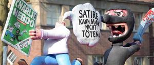 "Satire kann man nicht töten", steht in einer Sprechblase. Zu sehen sind eine Figur ohne Kopf, welche eine Ausgabe des Satiremagazins "Charlie Hebdo" in den Händen hält, und ein schwarz gekleideter "Terrorist" mit Schwert.