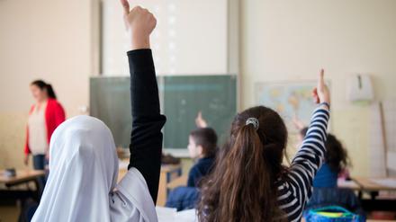 Zwei Mädchen, eine davon mit Kopftuch, sitzen in einer Klasse und melden sich.