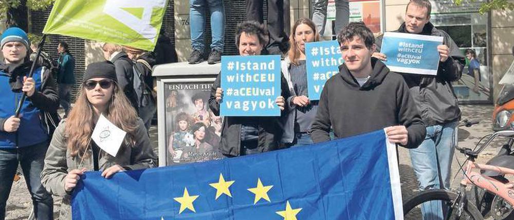 Jungen Menschen stehen am Rand einer Straße und halten Schilder mit der Aufschrift I stand with CEU hoch.