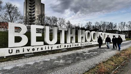 Vier Studierende gehen einen gepflasterten Weg entlang, parallel dazu ist der überdimensionale Schriftzug Beuth Hochschule zu sehen.