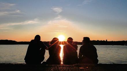 Jugendliche sitzen beim Hafenfest am Ufer des Tegeler Sees in Berlin. 