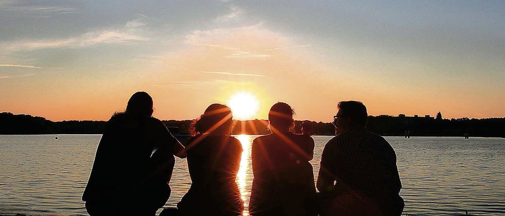 Jugendliche sitzen beim Hafenfest am Ufer des Tegeler Sees in Berlin.